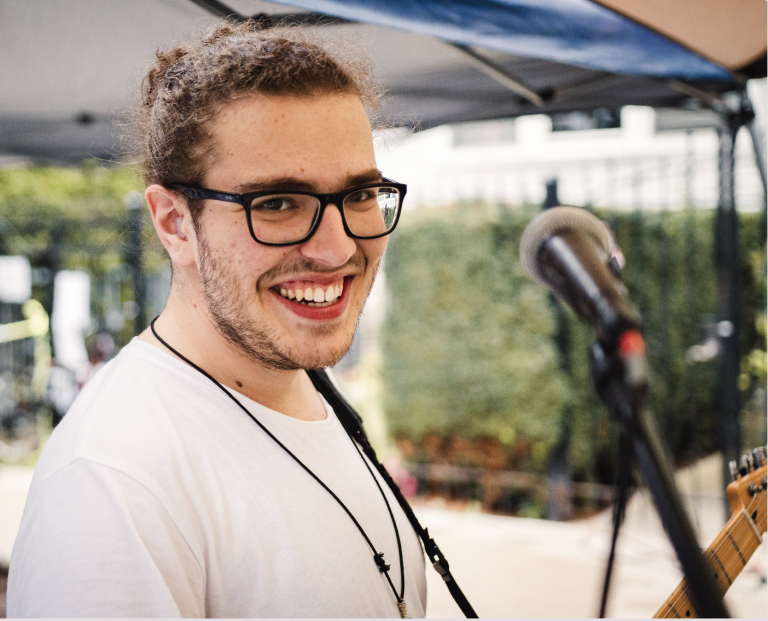 Bryan smiling at the camera near a microphone witrh a guitar on his shoulder